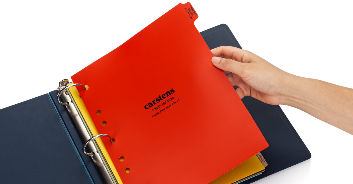 A woman in blue scrubs is sitting at a desk. On the desk is a binder with papers in the rings.