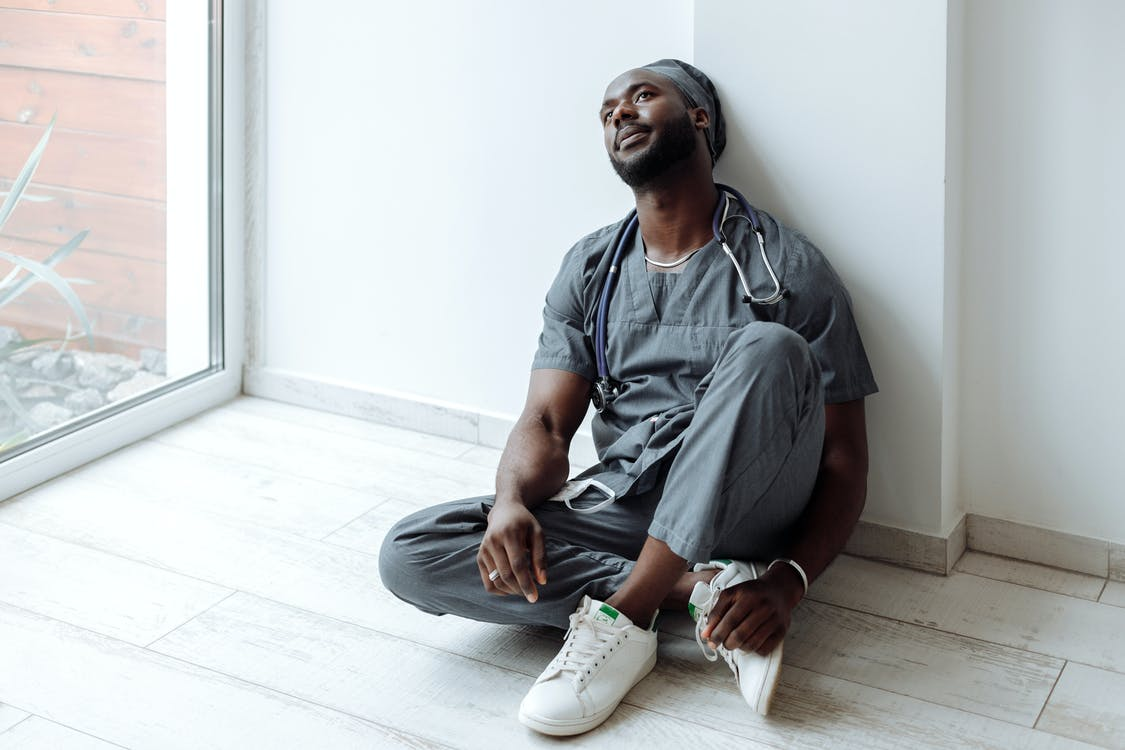 A male nurse sitting on the floor, suffering from the effects of alarm fatigue.