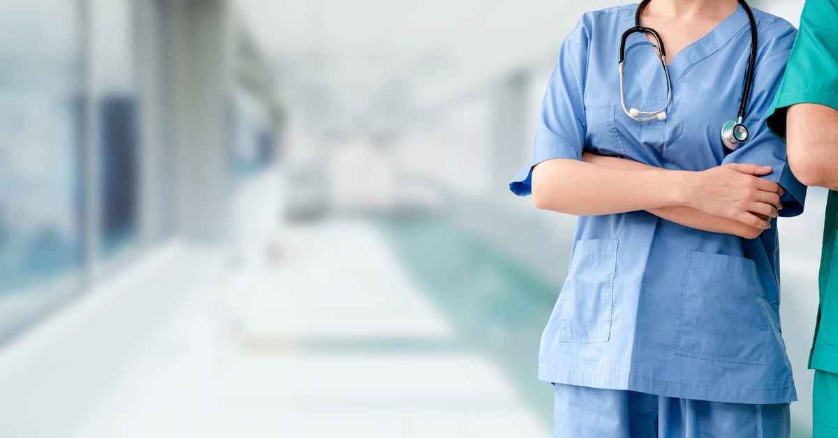 A woman is standing next to a man. They are both wearing blue scrubs and are both crossing their arms.