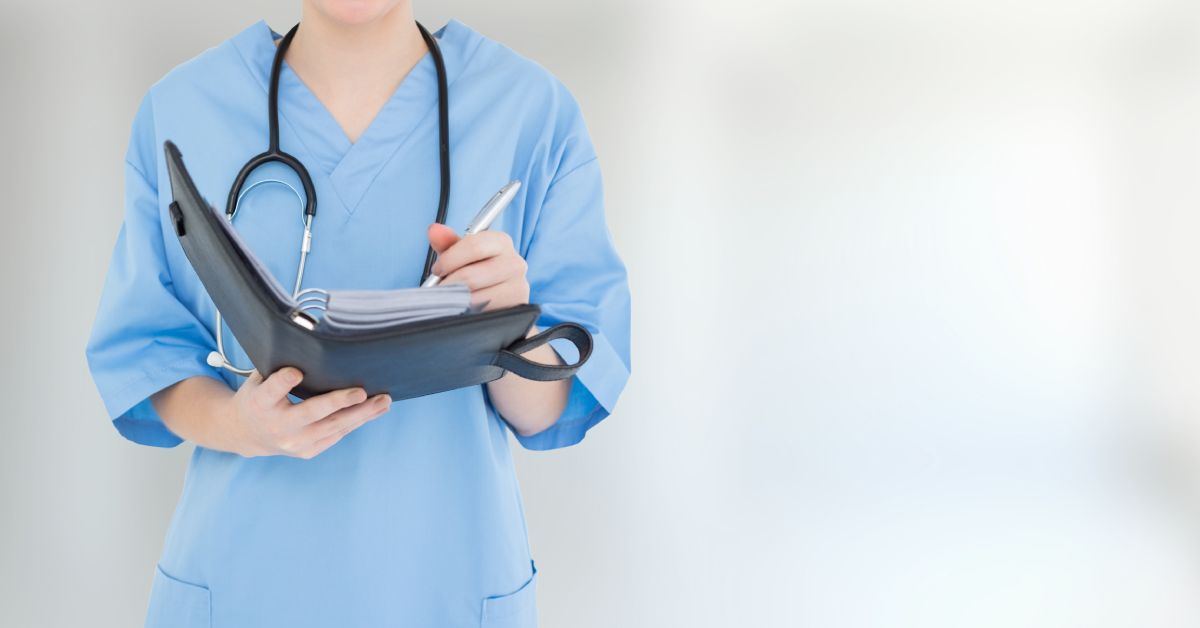 A woman in blue scrubs and with a stethoscope around her shoulders is holding a binder in her hands.