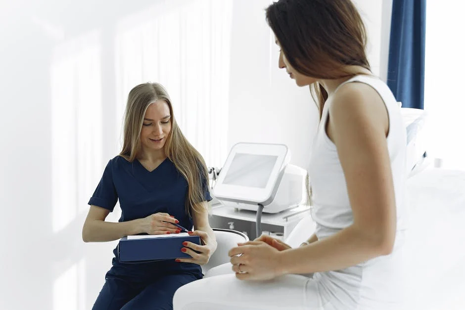 A nurse speaking with a female patient in a doctor’s office while taking notes on a chart.